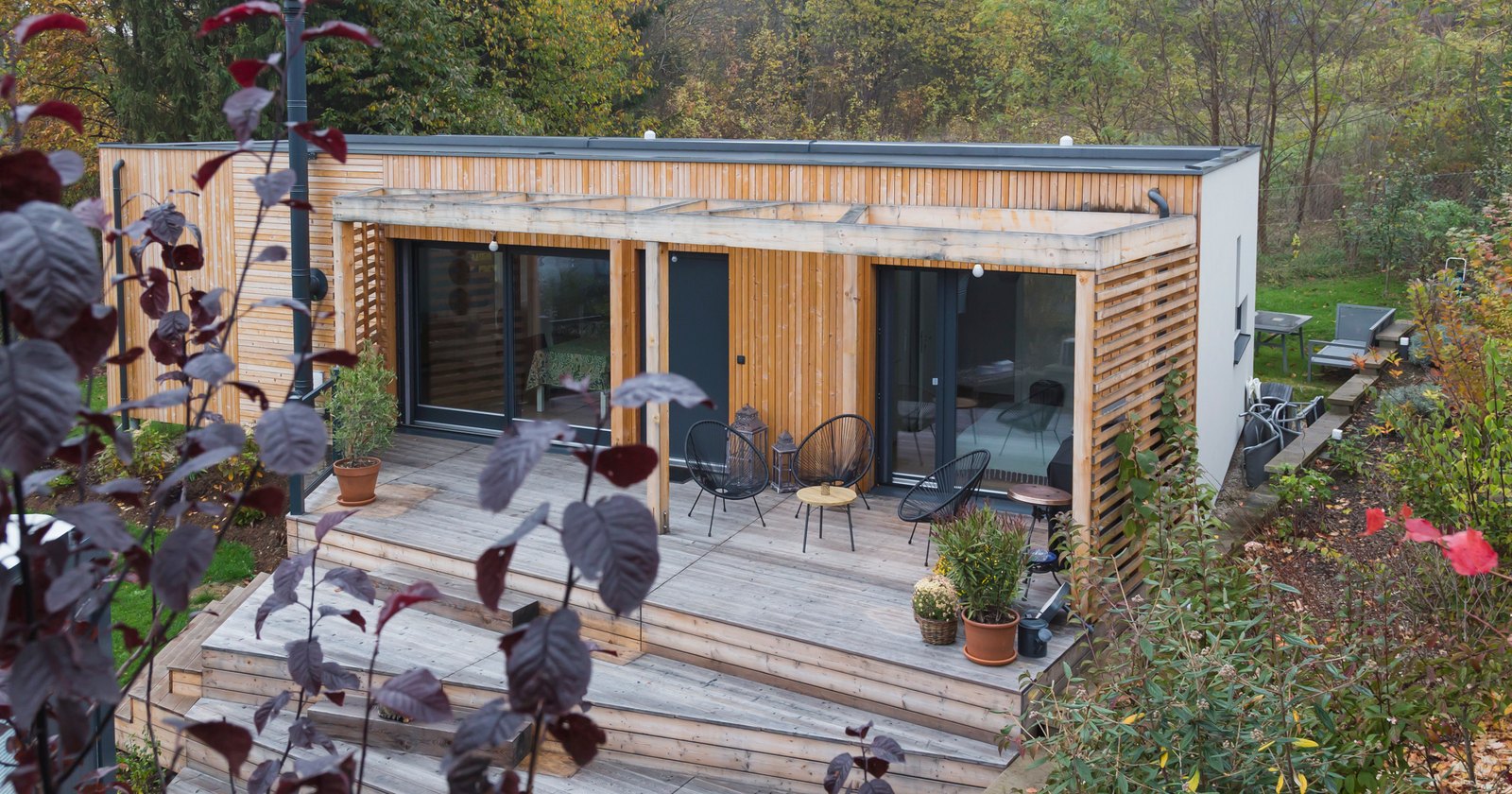 COMMOD HOUSE mit Holzfassade und Terrasse, umgeben von herbstlich gefärbten Pflanzen