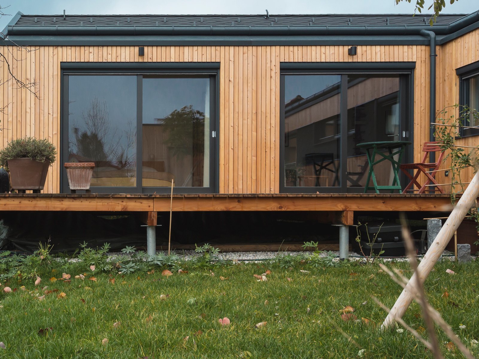 COMMOD HOUSE mit Holzfassade und großen Glasflächen über einer Terrasse, im Herbst
